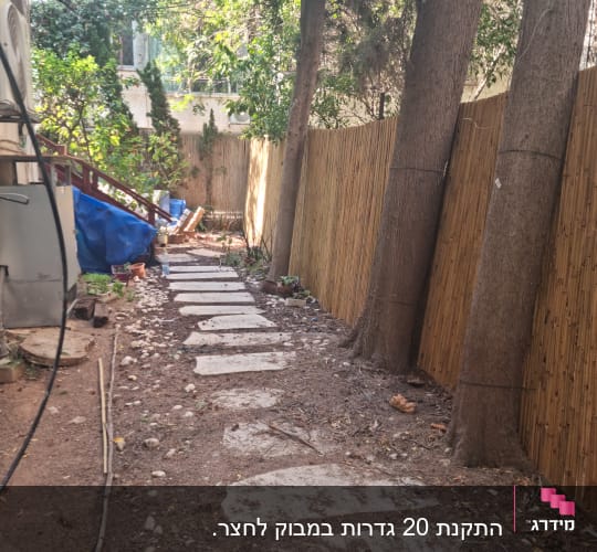 שביל אבני מדרך בגינה לצד גדר במבוק ועצים